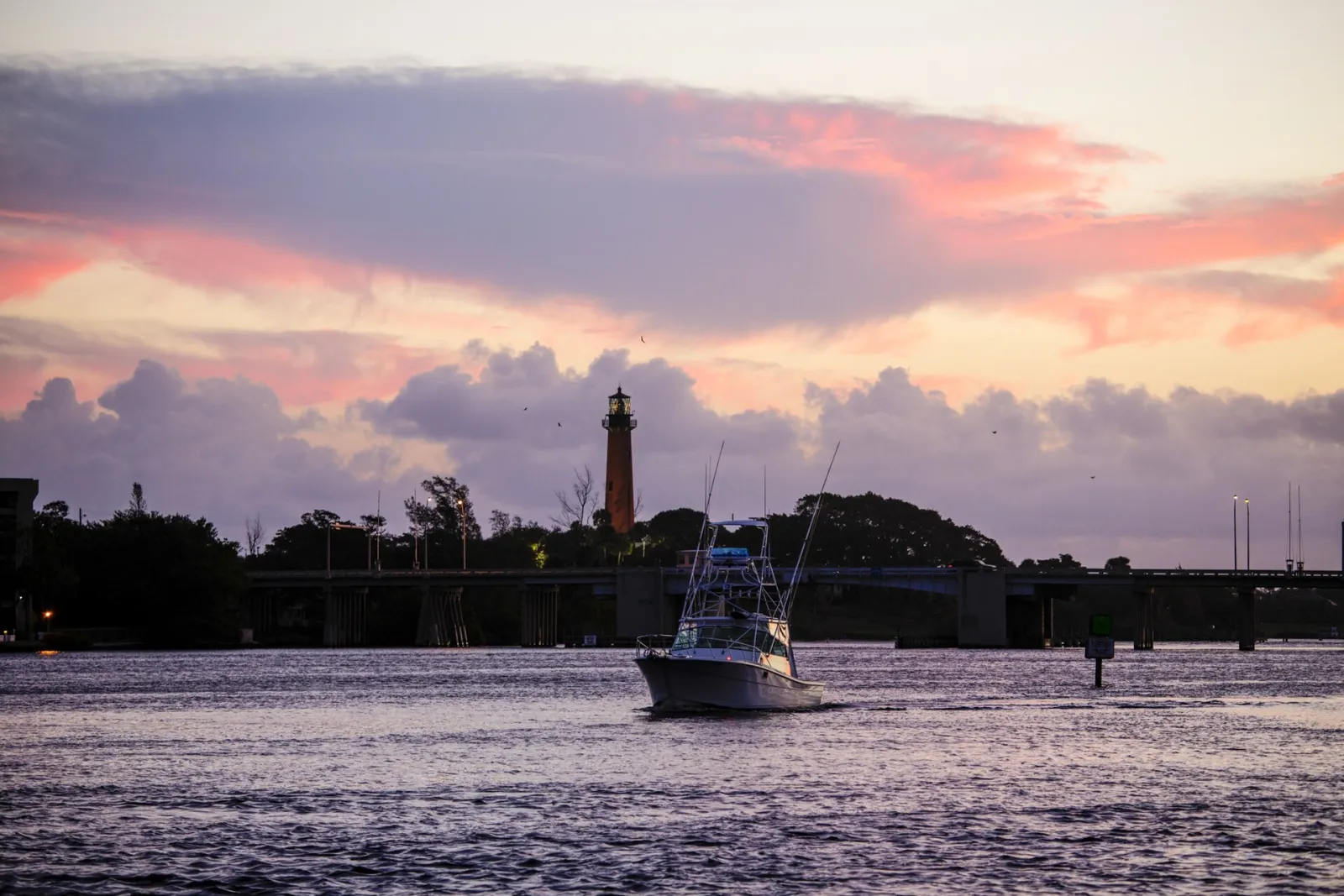 A fishing boat heads in at dusk with the Jupiter Inlet Lighthouse behind it.