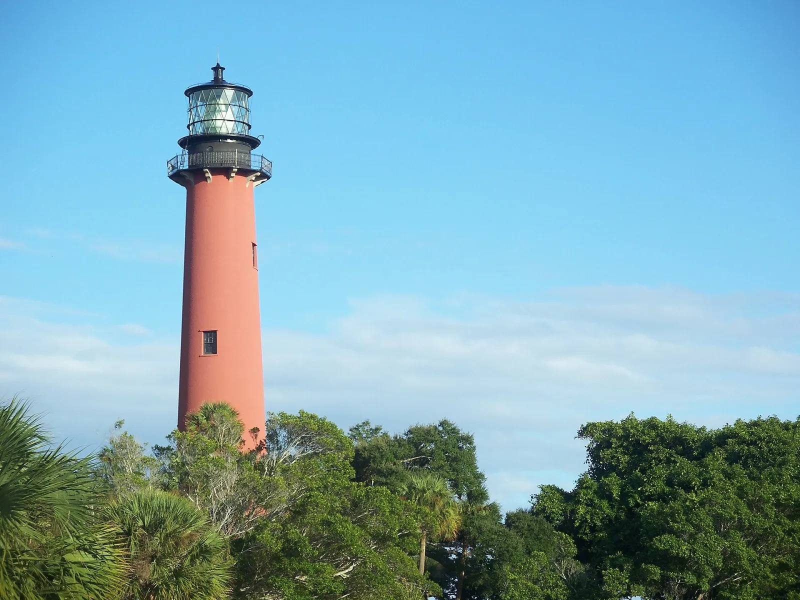 The red Jupiter Inlet Lighthouse rises above the trees at the mouth of the Loxahatchee River in Jupiter.